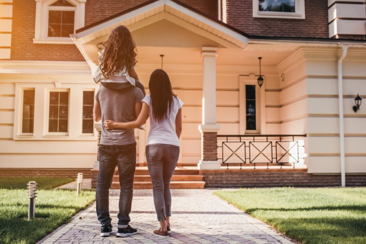 Back view of happy family is standing near their modern house.